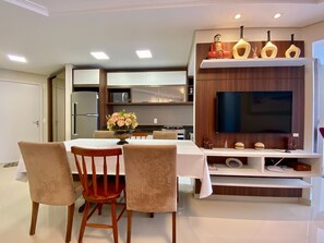 Una cocina moderna con televisor integrado, un comedor con sillas y un jarrón decorativo sobre la mesa.