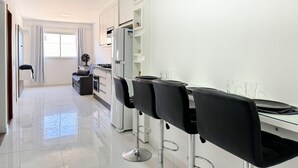 A modern kitchen with white cabinets, a dining area with black chairs, and a large window providing natural light.