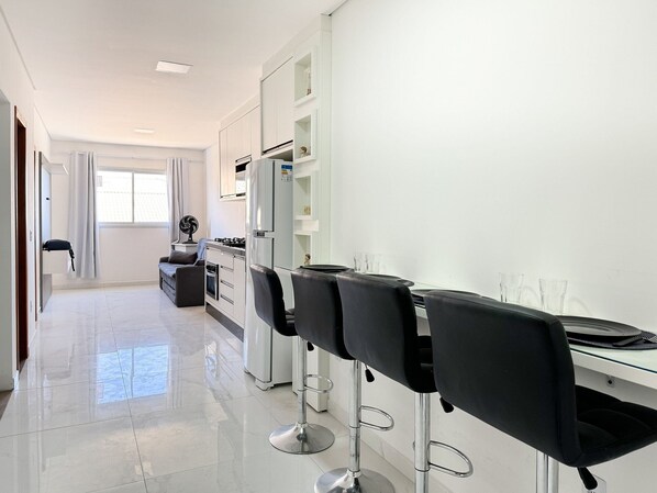 A modern kitchen with white cabinets, a dining area with black chairs, and a large window providing natural light.