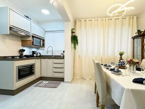 A modern kitchen with built-in appliances, a dining area with a table set for two, and a large window with curtains.