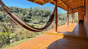 Eine Holzterrasse mit einer Hängematte, mit Blick auf eine üppige Landschaft und ein kleines Gebäude.