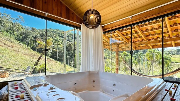 Ein Spa-Raum mit einer großen Badewanne, Holzbalkendecke und großen Fenstern mit Blick auf eine üppige Landschaft.