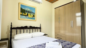A bedroom with a bed, a wooden wardrobe, a painting on the wall, and an air conditioning unit.
