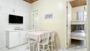 A room with a TV, a table with chairs, a bunk bed, and a wall with a cactus poster.