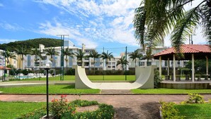 A pathway leading to a modern building with a unique curved structure, surrounded by well-maintained gardens and palm trees. - Refúgio Terra do Sol - NIN009 (Florianópolis)
