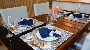 A dining table set with plates, napkins, and glassware, with a wooden wall and a microwave in the background. - Refúgio Terra do Sol - NIN009 (Florianópolis)