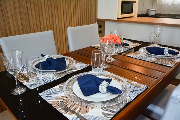 A dining table set with plates, napkins, and glassware, with a wooden wall and a microwave in the background.