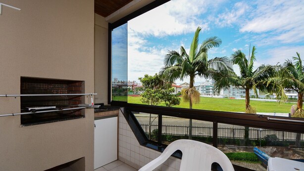 A balcony with a view of a grassy area, palm trees, and a distant building. - Refúgio Terra do Sol - NIN009 (Florianópolis)