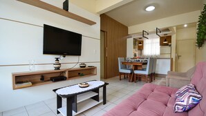 A modern living room with a flat-screen TV, a wooden shelf, a small table, and a pink sofa. - Refúgio Terra do Sol - NIN009 (Florianópolis)