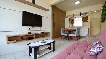Uma sala de estar moderna com uma TV de tela plana, uma estante de madeira, uma mesinha e um sofá rosa.