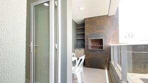 Un balcon moderne doté d’une porte-fenêtre coulissante, d’un petit coin salon avec une chaise blanche et d’un barbecue encastré dans le mur.