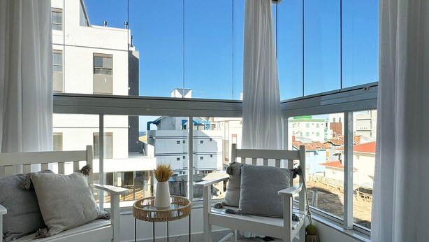 A balcony with white furniture, including two chairs and a small table with a vase.