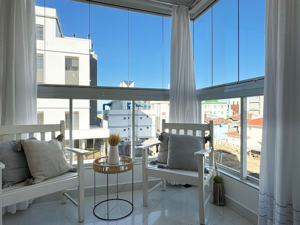 Un balcon agrémenté de meubles blancs, notamment deux chaises et une petite table sur laquelle est posé un vase.