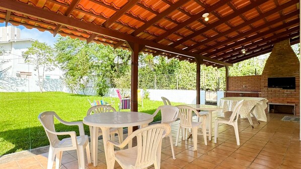 Une terrasse extérieure dotée d’un four en briques et d’un espace salon couvert avec des chaises en plastique et une table.
