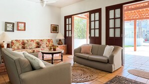 Una sala de estar con sofá, sillones, una mesa de centro y una puerta que da al exterior.