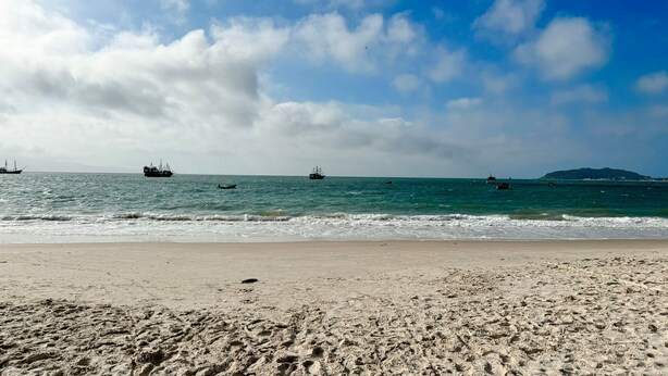 Una playa con huellas visibles y barcos en el agua.