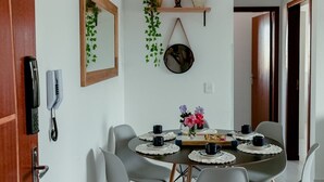 A dining area with a round table set for four, surrounded by chairs. There is a mirror on the wall, a telephone, and a shelf with decorative items.