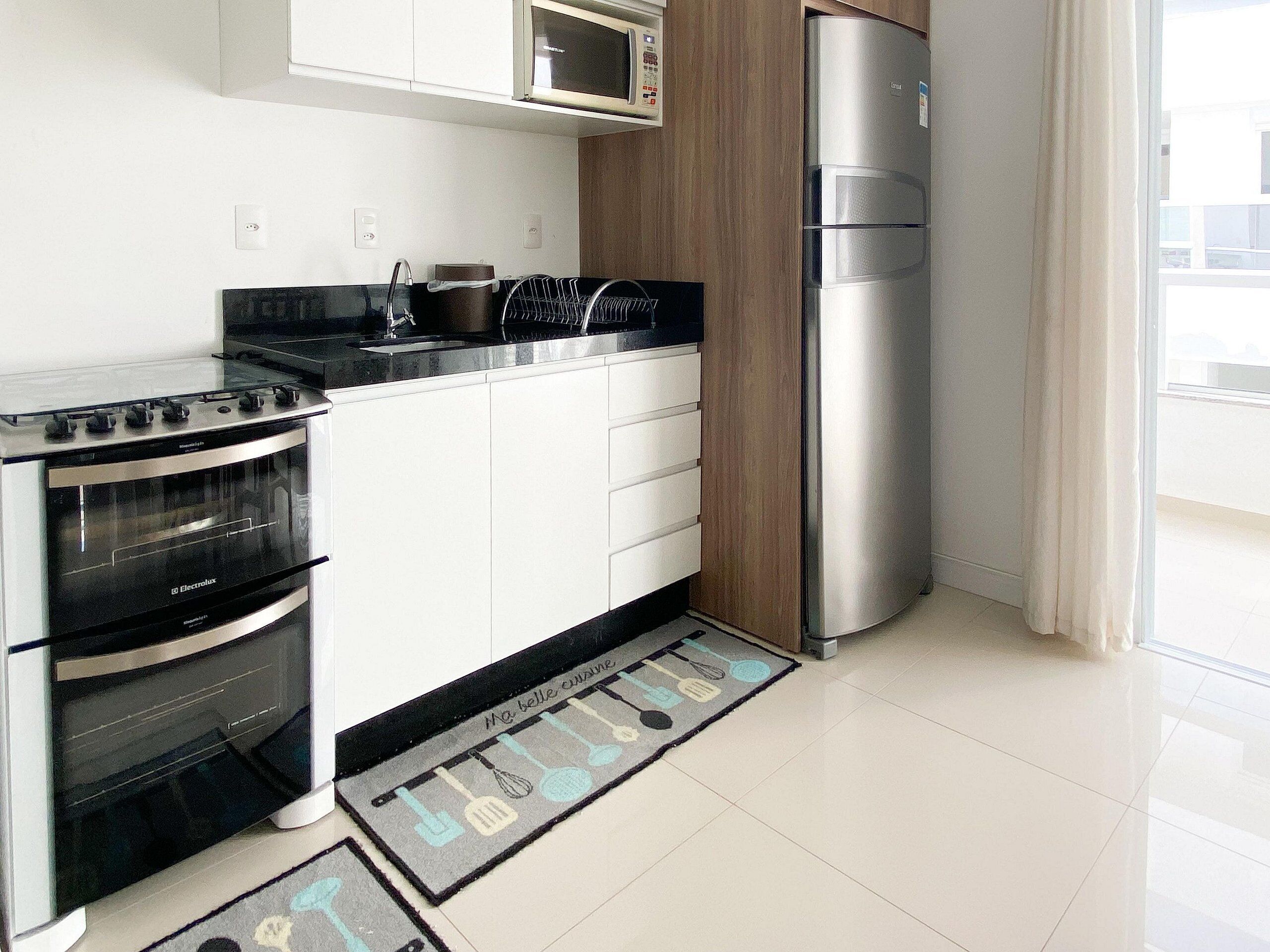 Uma cozinha moderna com frigorífico de aço inoxidável, forno embutido e micro-ondas.