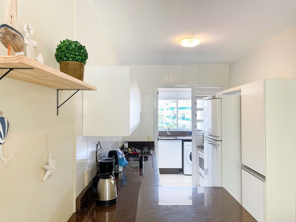 A modern kitchen with white cabinets, a stainless steel kettle, and a built-in oven.