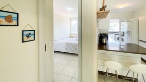 Una habitación de hotel compacta con una cama, una kitchenette pequeña y una zona de comedor con dos taburetes.