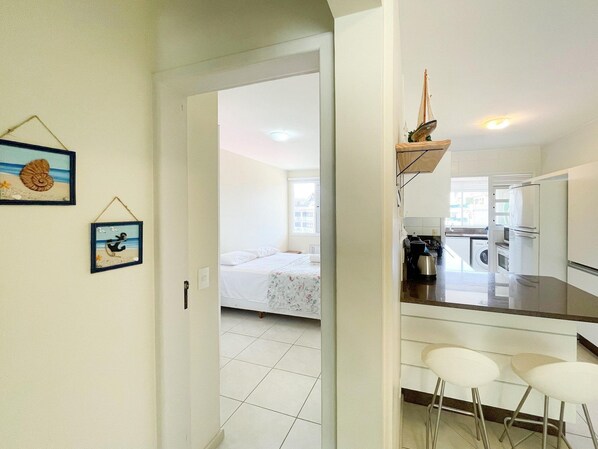 A compact hotel room with a bed, a small kitchenette, and a dining area with two stools.