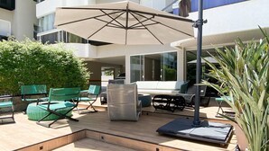 Un espacio al aire libre con patio, sofá, sillas, una mesa y un paraguas.
