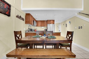 A dining area with a wooden table and chairs, a kitchen in the background, and a framed picture on the wall. - NEW! CreekSide #3 (3-Bedroom Home) - Pets Allowed by Bear Valley Vacation Rentals (Bear Valley)