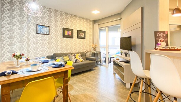 A modern living room with a dining area, a sofa, a TV, and a coffee station. - Resid. Clube Mar Grosso - Laguna - LAG208 (Laguna)
