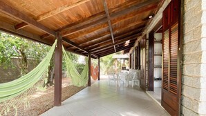 A covered outdoor area with a hammock, tiled floor, and stone walls.