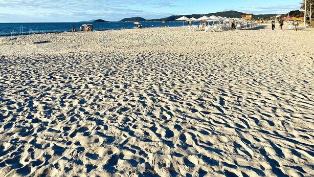 A wide sandy beach with umbrellas and beach chairs, a clear blue sky, and distant hills. - Casa de Pedra - Canasvieiras - NDI002 (Florianópolis)