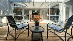 Eine Terrasse im Freien mit Korbmöbeln und einem Tisch in der Mitte, umgeben von einer Glaskonstruktion.