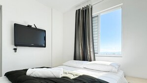 Ein Hotelzimmer mit Bett, Flachbildfernseher an der Wand, einem Fenster mit Vorhängen und Blick auf die Stadt.