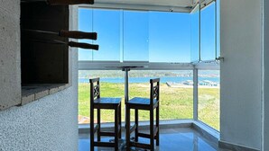 A room with a large window offering a view of a body of water and distant land. There are two wooden chairs and a table in the room. - Resid. Clube Mar Grosso - Laguna - LAG801 (Laguna)