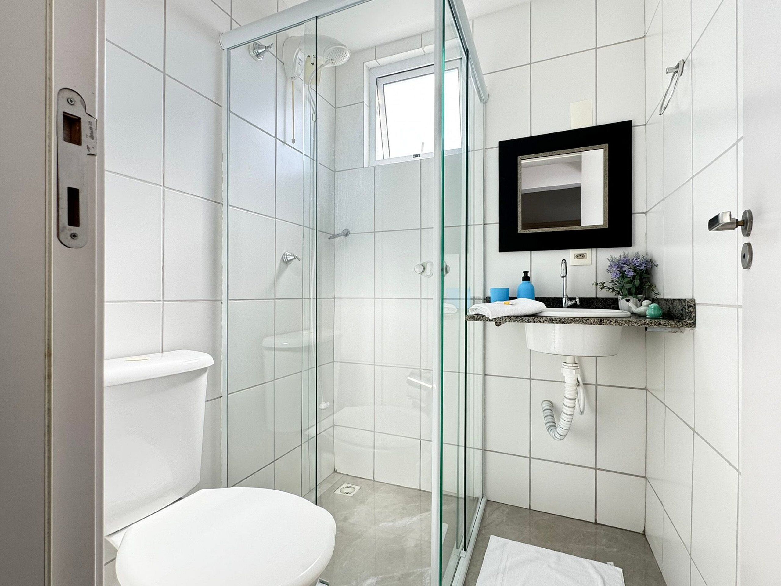 A modern bathroom with a glass-enclosed shower, a white toilet, a sink with a black countertop, and a mirror above the sink.