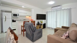 Una sala de estar moderna con un sofá, un sillón reclinable, un televisor de pantalla plana y una zona de cocina con microondas y refrigerador.