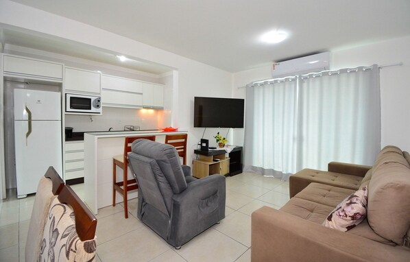 Una sala de estar moderna con un sofá, un sillón reclinable, un televisor de pantalla plana y una zona de cocina con microondas y refrigerador.