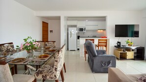 Una sala de estar moderna con comedor, cocina y un televisor de pantalla plana montado en la pared.