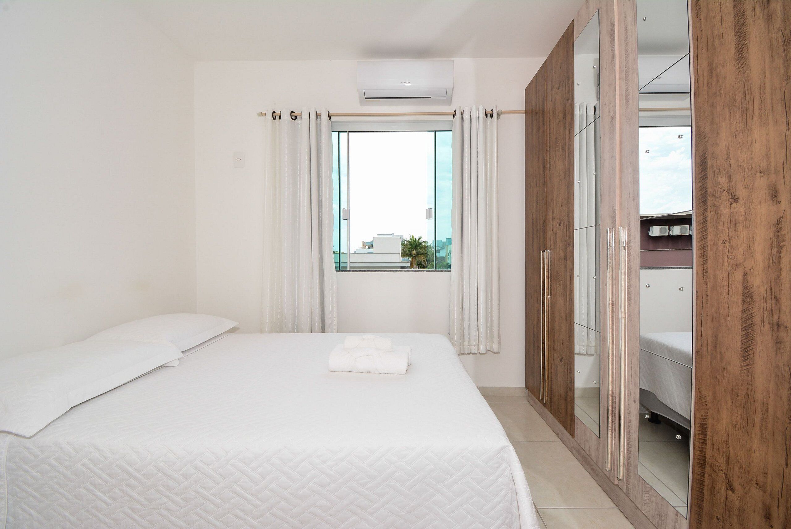 Ein Hotelzimmer mit einem Bett, einem Vorhangfenster, einer Klimaanlage und einem Schrank mit Spiegel.