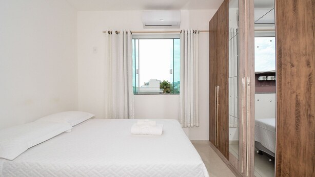 Una habitación de hotel con cama, ventana con cortinas, aire acondicionado y un armario con espejo.