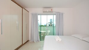 Habitación de hotel con cama, armario, balcón con mesa y sillas, y vista a edificios.