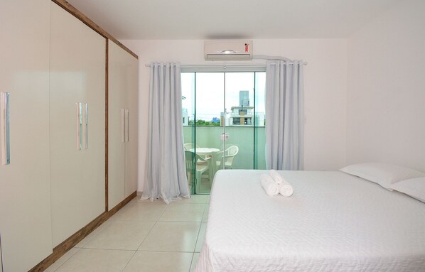 Habitación de hotel con cama, armario, balcón con mesa y sillas, y vista a edificios.