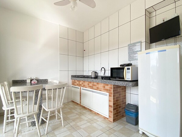 A kitchen with white cabinets, a granite countertop, a microwave, a kettle, and a refrigerator. - Residencial Verdes Mares (Bombinhas)