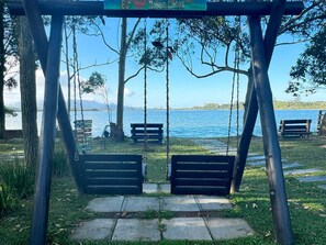 Un conjunto de columpios con bancos, vista despejada de un lago y un cartel con indicaciones.