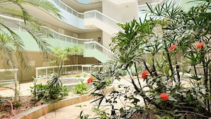 A multi-level atrium with a central staircase, surrounded by lush greenery and red flowers.