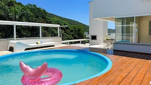 A swimming pool with a wooden deck, a white lounge chair, and a glass-enclosed room.