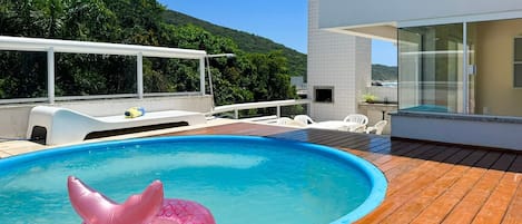 A swimming pool with a wooden deck, a white lounge chair, and a glass-enclosed room.
