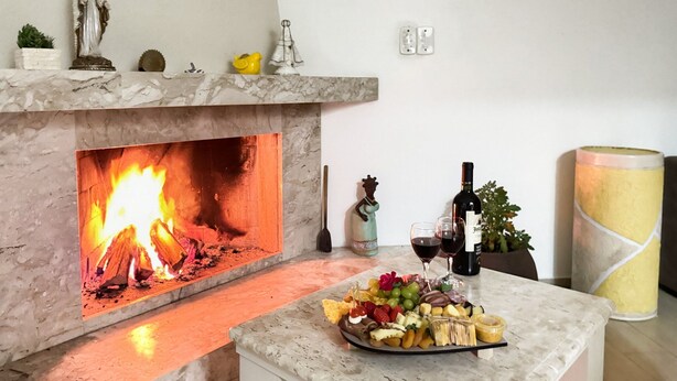 Una sala de estar acogedora con chimenea, una mesa de centro de mármol con una bandeja de frutas y una botella de vino.
