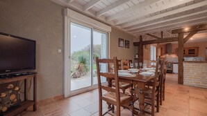 Comedor con una mesa grande dispuesta para seis, sillas de madera y un televisor sobre un mueble.