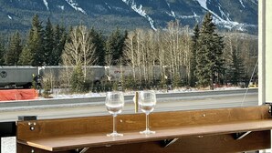 A wooden bench with two glasses on it, overlooking a snowy mountain range and a road with a truck in the background. - Stunning Views | Brand-New Townhouse | Sleeps 11 AC +Hot Tub (Harvie Heights)