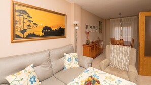 Un salon avec un canapé, un fauteuil et un tableau représentant un coucher de soleil.